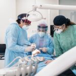 Equipo quirúrgico con bata esteril y lupas colocando un implante dental en un campo esteril