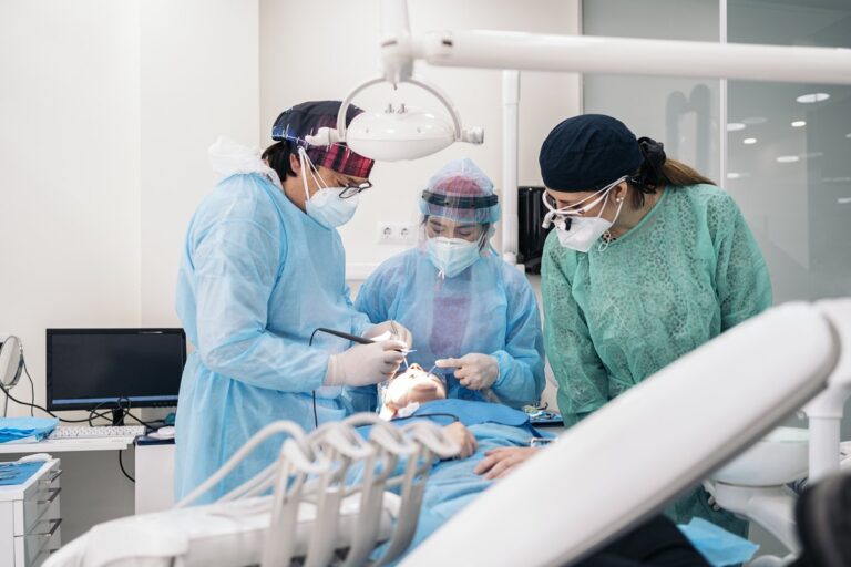 Equipo quirúrgico con bata esteril y lupas colocando un implante dental en un campo esteril