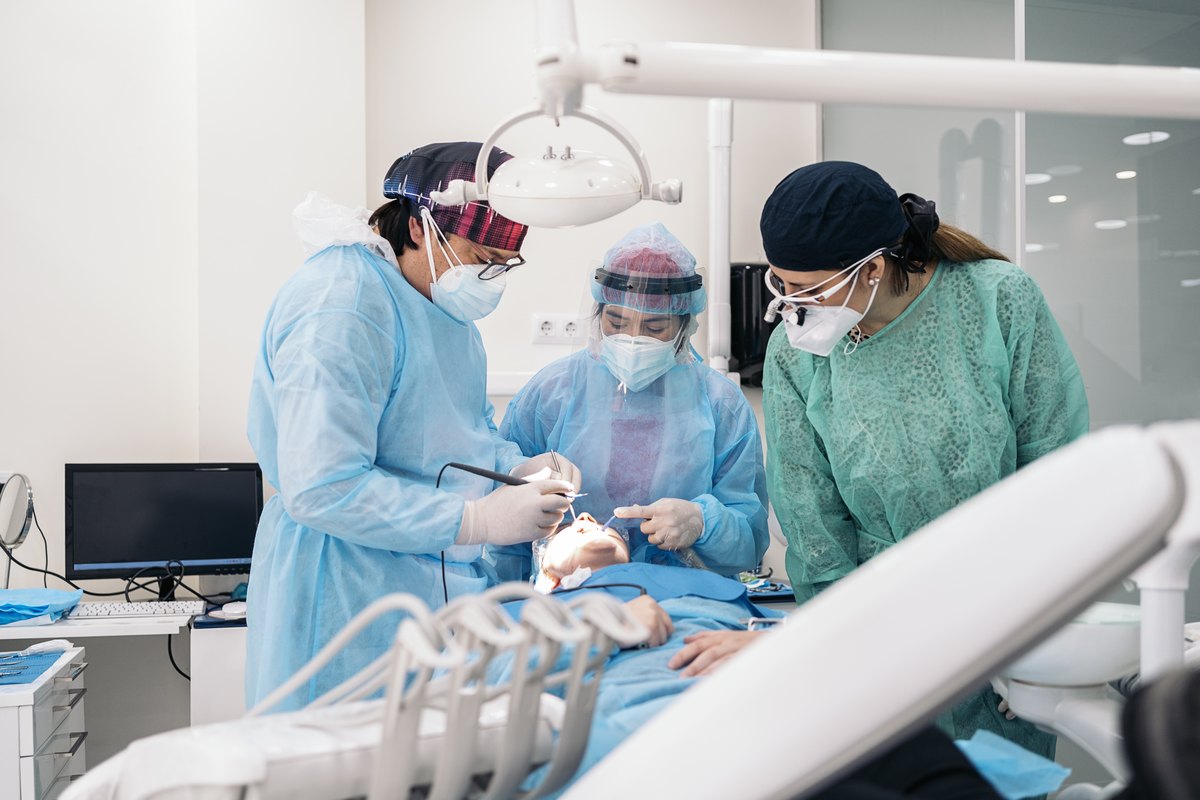 Equipo quirurgico con bata esteril y lupas colocando un implante dental en un campo esteril
